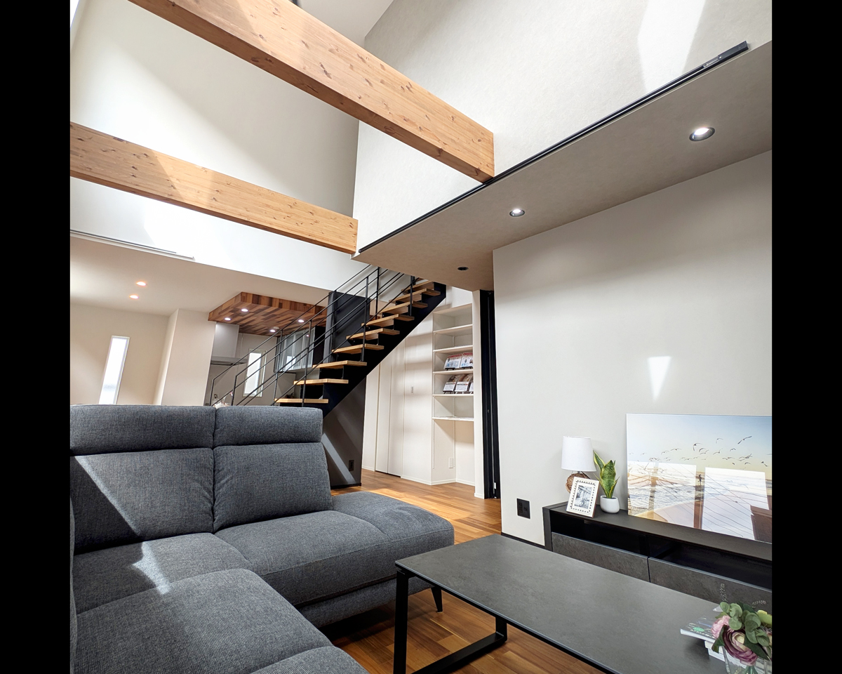 『開放感あふれるリビング吹き抜け』<br />
大きな窓からたっぷり光が差し込む吹き抜けリビングは、家全体に開放感をもたらす特別な空間。時間帯や季節ごとに移ろう光の表情を楽しめ、家族の集まるリビングに豊かな変化を与えます。<br />
上部の化粧梁や鉄骨階段との組み合わせがデザインのアクセントとなり、開放感とスタイリッシュさを両立。広がりのある空間ながら、エリアワン標準の高気密・高断熱仕様と第一種熱交換型換気システムにより、快適な室温環境を一年中保てます。