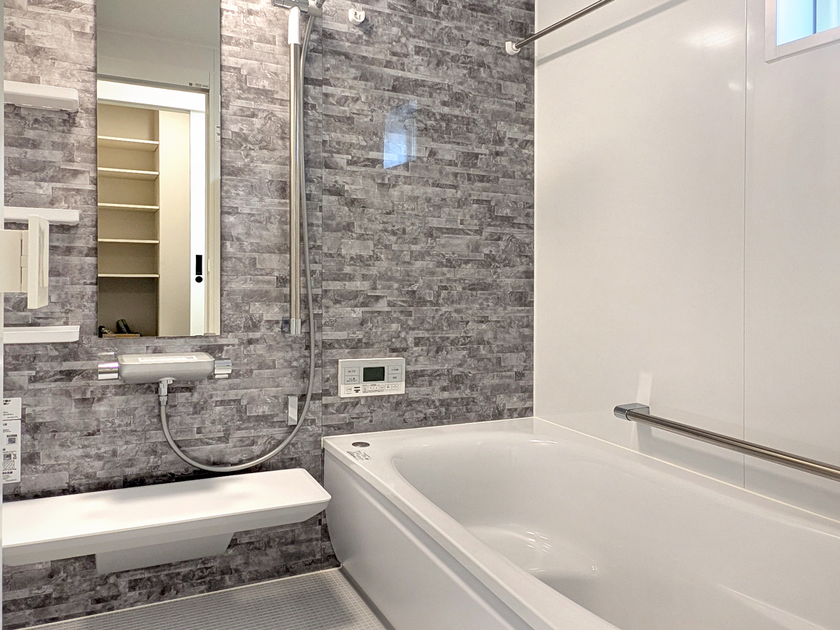 『脱衣室つきバスルーム』<br />
グレーのアクセントパネルが落ち着きと上質感を演出するバスルーム。隣接する脱衣室と直結しているので、入浴後の着替えや洗濯の動線もスムーズです。<br />
ユニットバスはTOTO「サザナ」を採用。W断熱構造のほっカラリ床で、冬でもヒヤッとしない快適な足ざわり。翌朝には床がカラリと乾くので、お掃除の手間も軽減されます。<br />
快適性と家事ラク性能を兼ね備えた、エリアワン注文住宅の標準仕様バスルームを、ぜひモデルハウスでご見学ください。