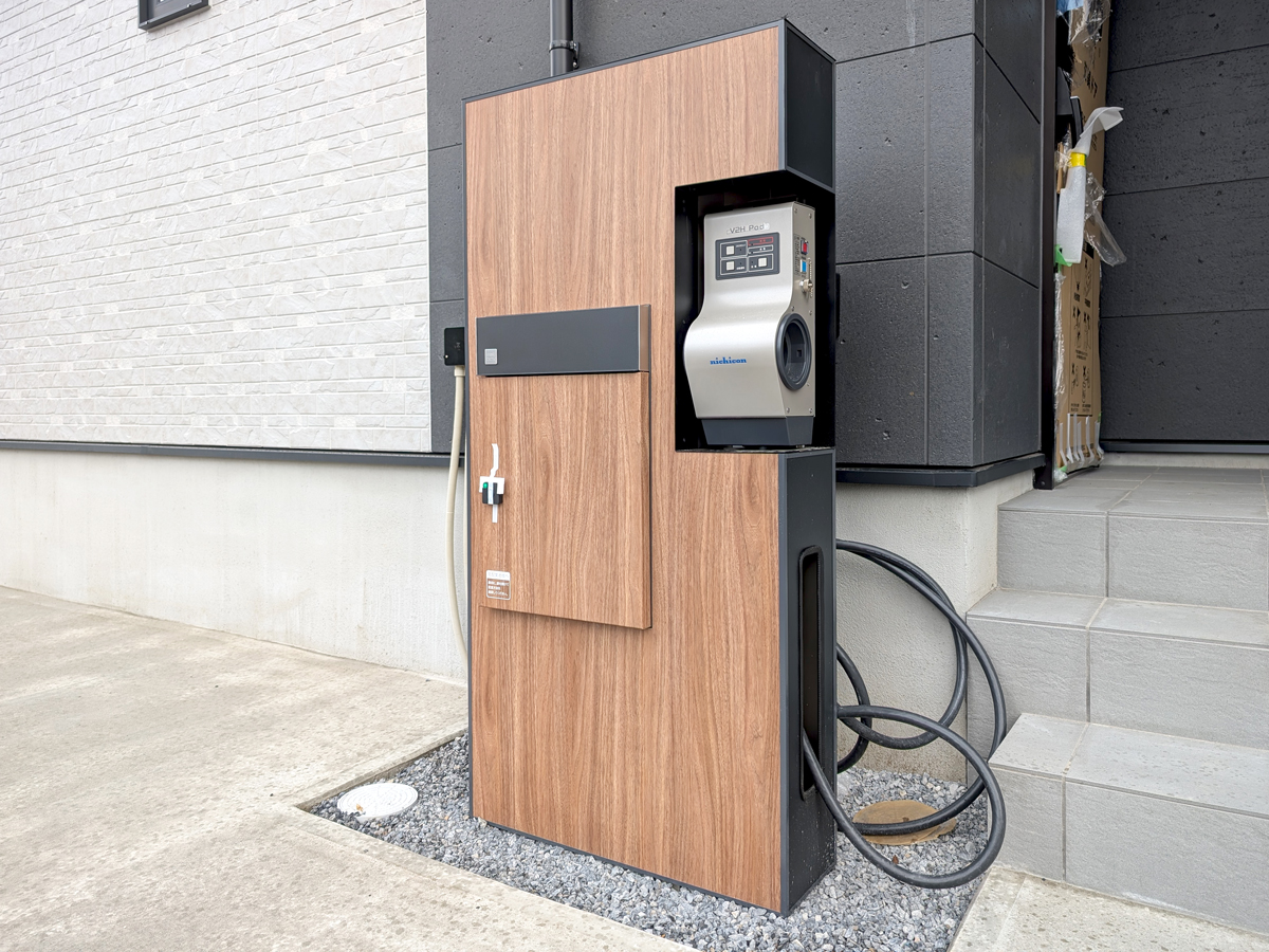 『宅配ボックス付き機能門柱（V2H対応）』<br />
今回のモデルハウスにもV2H機器を導入。エクステリア大手のタカショー、V2H分野のリーディング企業ニチコン、専門商社ユアサ商事が共同開発した製品で、多機能を一体化したコンパクト設計です。宅配ボックス、郵便ポスト、EV・PHEVの充電も出来るV2Hシステムをスリムにまとめた、外構デザインに自然に溶け込む木目調仕上げが目を惹きます。<br />
停電などの非常時には、車に蓄えた電力を家じゅうで使える全負荷対応（最大5.9kW）を実現。エアコンなど200V機器も稼働でき、もしもの時も安心です。